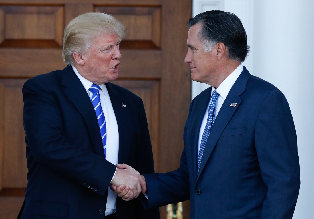 President Donald Trump (left) shakes hands with Senator Mitt Romney of Utah (right). Sen, Romney has a subtle smile, his face seems plased and Pres. Trump has a gaping mouth and odd expression,